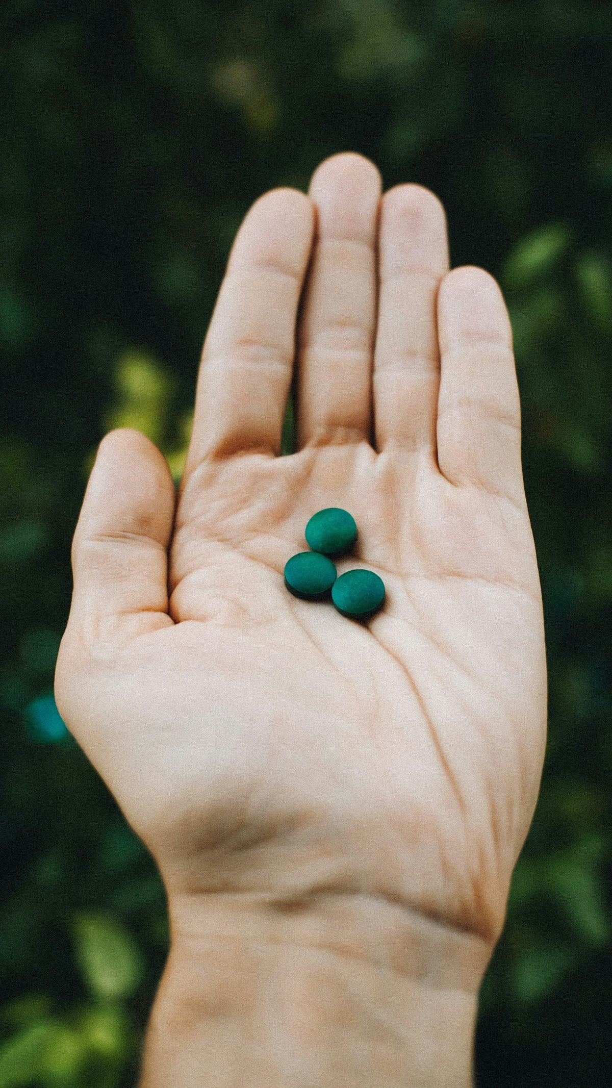 Mano sosteniendo cápsulas verdes de espirulina, un superalimento natural en formato suplemento